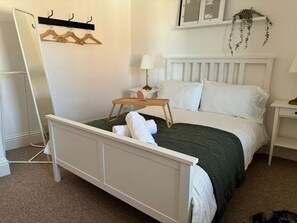 A neatly made bed with a white headboard, a bedside table with a lamp, and a wall-mounted plant. - Town Centre Flat For Two Adults (Perth and Kinross)