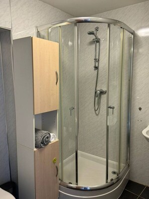A corner shower enclosure with a glass door, a wooden cabinet with a towel, and a white sink. - Town Centre Flat For Two Adults (Perth and Kinross)