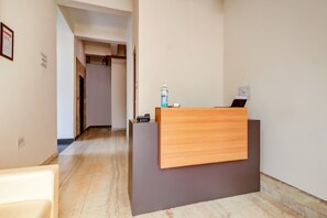 A reception desk with a wooden panel and a grey counter, a hand sanitizer dispenser, and a small black device on the counter. - Hotel O Hotel Outline (Ranchi)