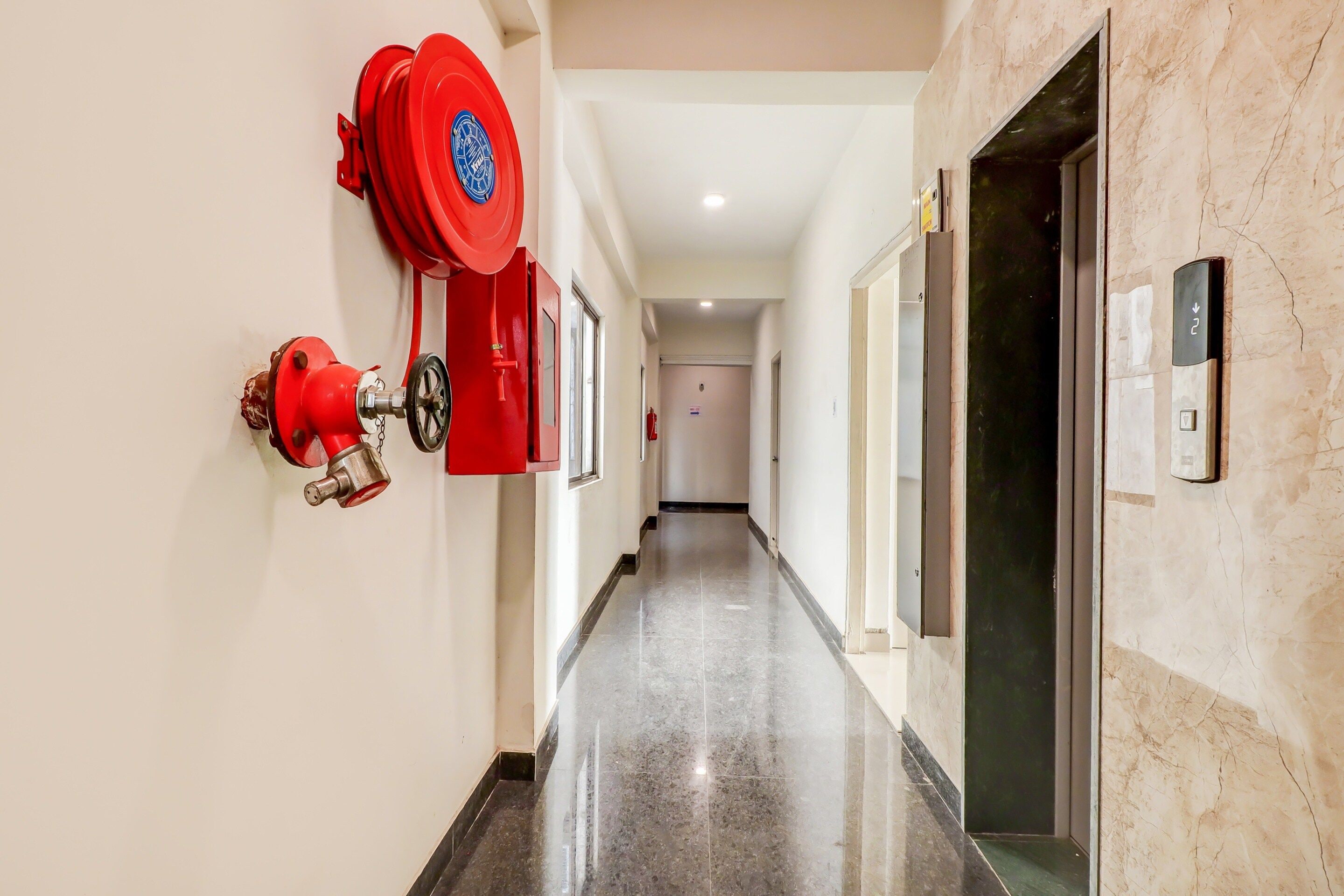 A hallway with a red fire extinguisher mounted on the wall, a door with an elevator sign, and a marble floor.
