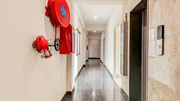 A hallway with a red fire extinguisher mounted on the wall, a door with an elevator sign, and a marble floor.