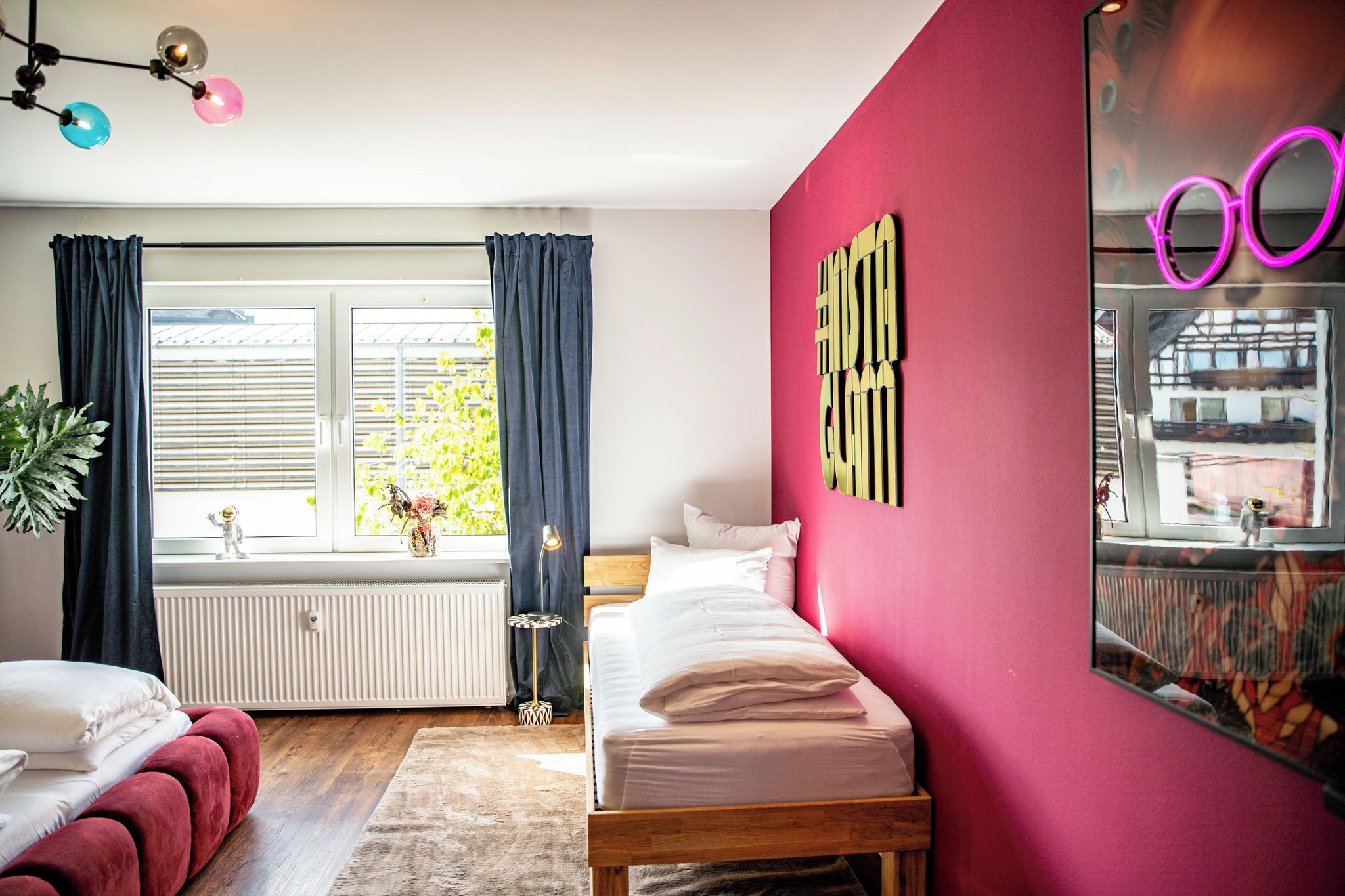 Un dormitorio con cama, ventana con cortinas, radiador y espejo con luz de neón.