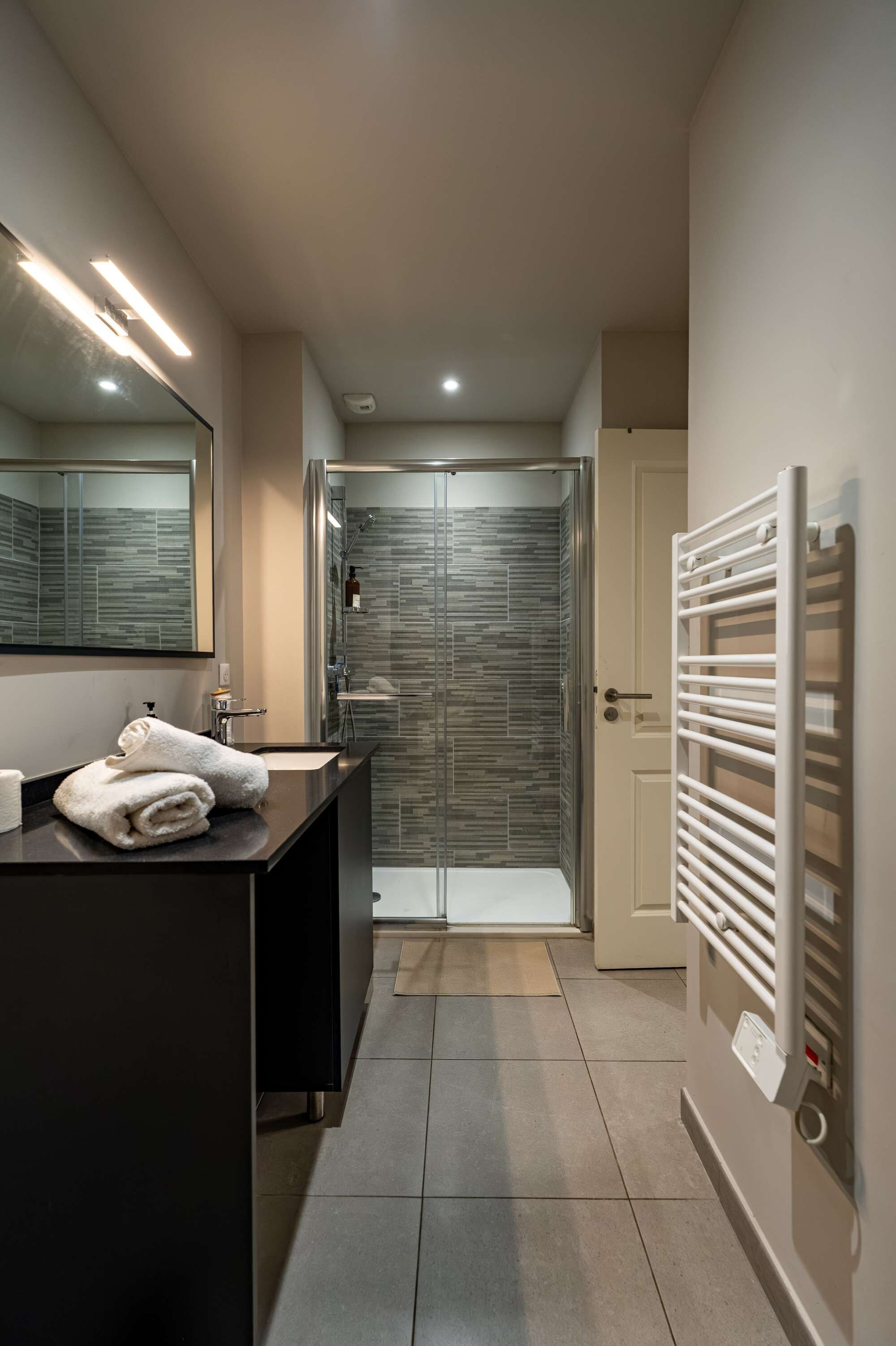 Un baño moderno con un mostrador oscuro, cabina de ducha con vidrio y una toalla blanca.