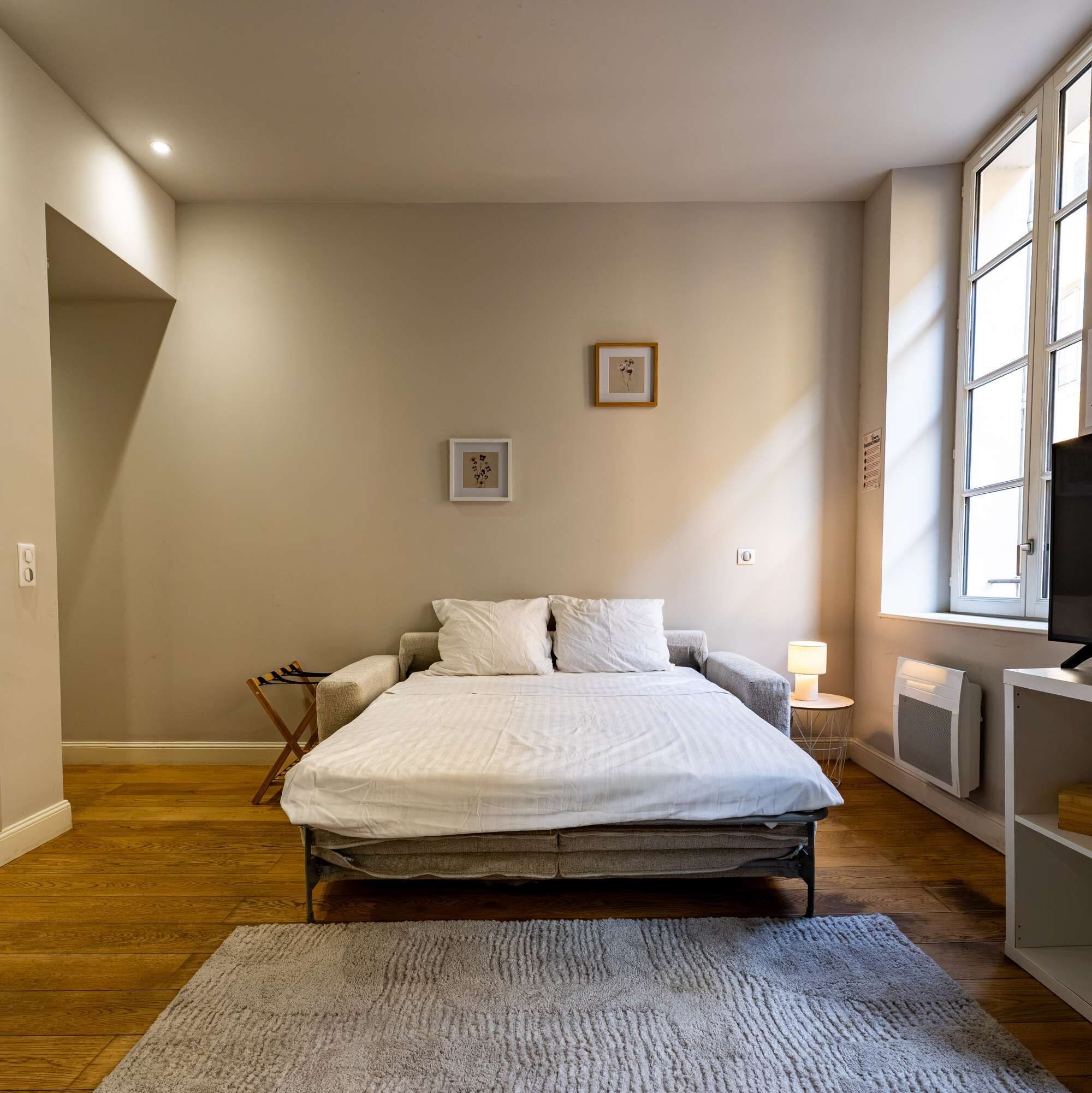 Un dormitorio con una cama, una silla, una mesita de noche con una lámpara y una ventana.