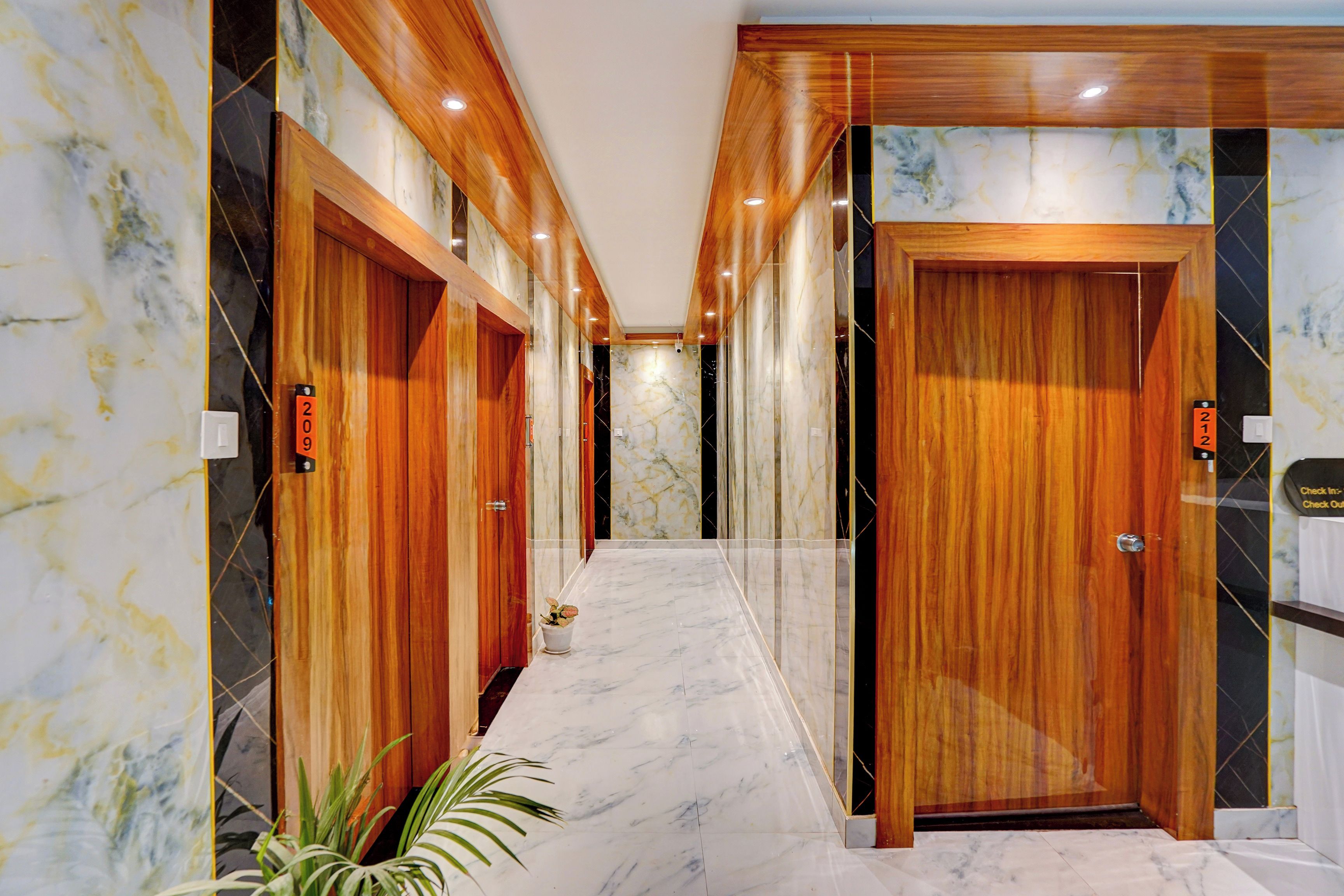 Un pasillo de hotel con puertas de madera, paredes de mármol y una planta en maceta.