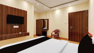 A hotel room with a bed, a TV mounted on the wall, a wooden wardrobe, a desk with a chair, and a door.