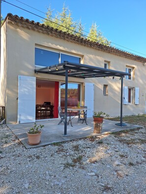 Ein Gebäude mit überdachter Terrasse, einem Tisch mit Stühlen und Topfpflanzen.