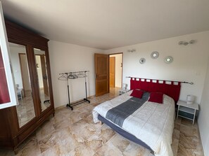 A bedroom with a bed, a wooden wardrobe, a clothing rack, and a door leading to another room. - Holiday home 'Gîte Les Piboules' with Mountain View, Wi-Fi and Air Conditioning (Caseneuve)