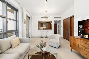 A modern living room with a sofa, armchair, coffee table, and a TV on a wooden cabinet. - FIRST CLASS | 1BR | Elegant Dubai Skyline (Downtown)