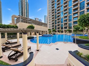 A swimming pool area with lounge chairs, a pergola, and high-rise buildings in the background. - FIRST CLASS | 1BR | Luxe Burj & City View (Downtown)