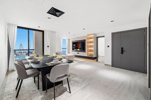 A modern living room with a dining area, a large flat-screen TV, and a view of a bridge and water. - FIRST CLASS | 3BR | Near JBR Beach | Ain Views (JBR)