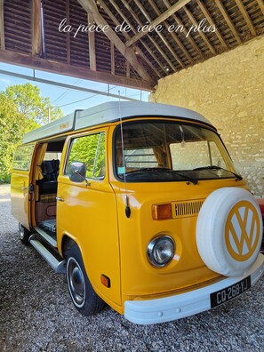 A yellow Volkswagen camper van parked under a wooden structure with a gravel ground. - Just an hour from Paris, a spacious home perfect for family get-togethers (or working from home)... (Guainville)