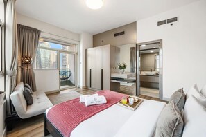 A modern hotel room with a bed, a seating area, a bathroom, and a balcony with a city view. - FIRST CLASS | 2BR | Prime Location | Skyline Views (Dubai)