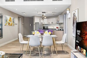 A modern kitchen with a dining area, a TV, and artwork on the walls. - FIRST CLASS | 2BR | Prime Location | Skyline Views (Dubai)