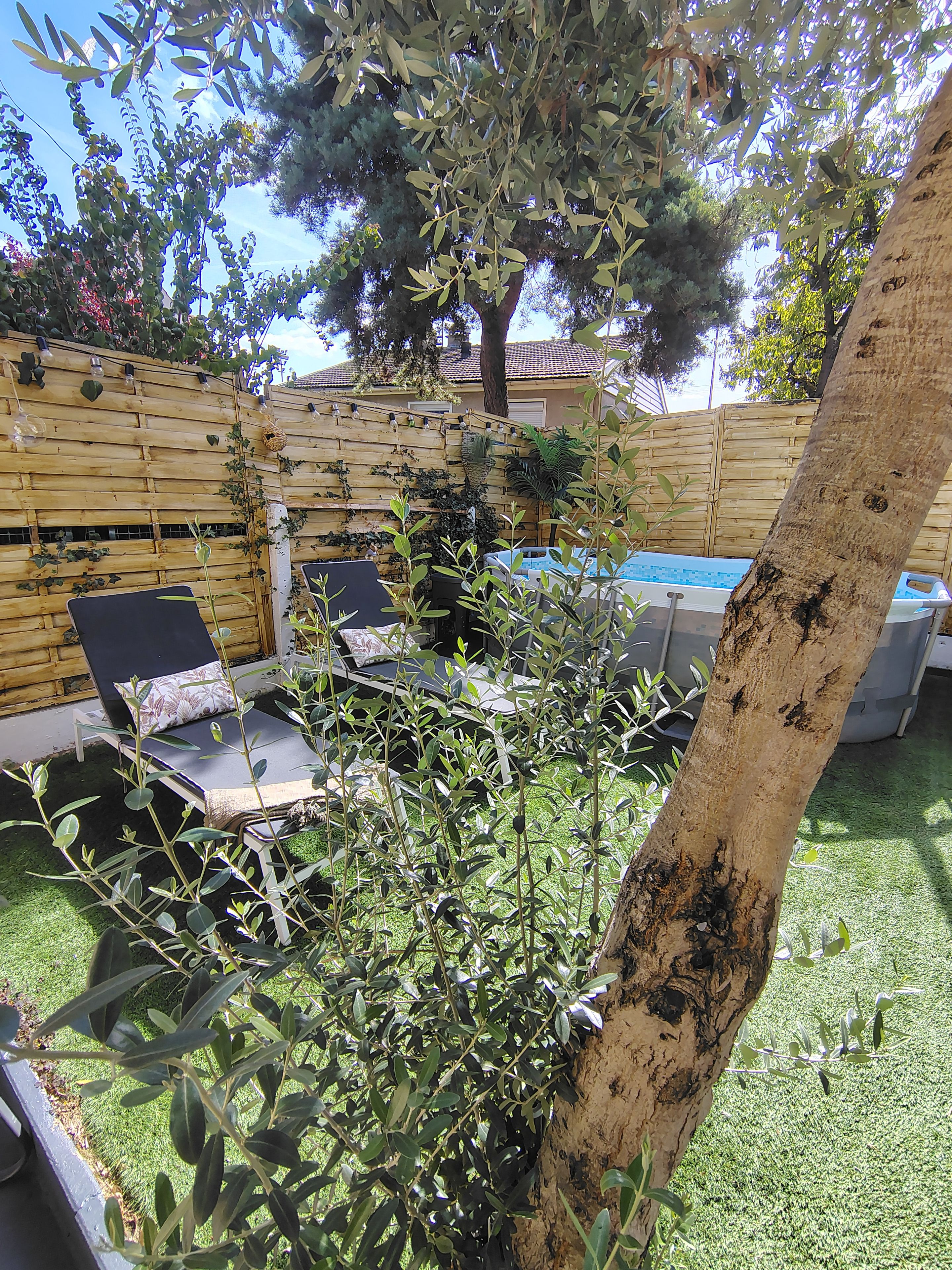 A backyard with a wooden fence, a pool, and outdoor furniture.