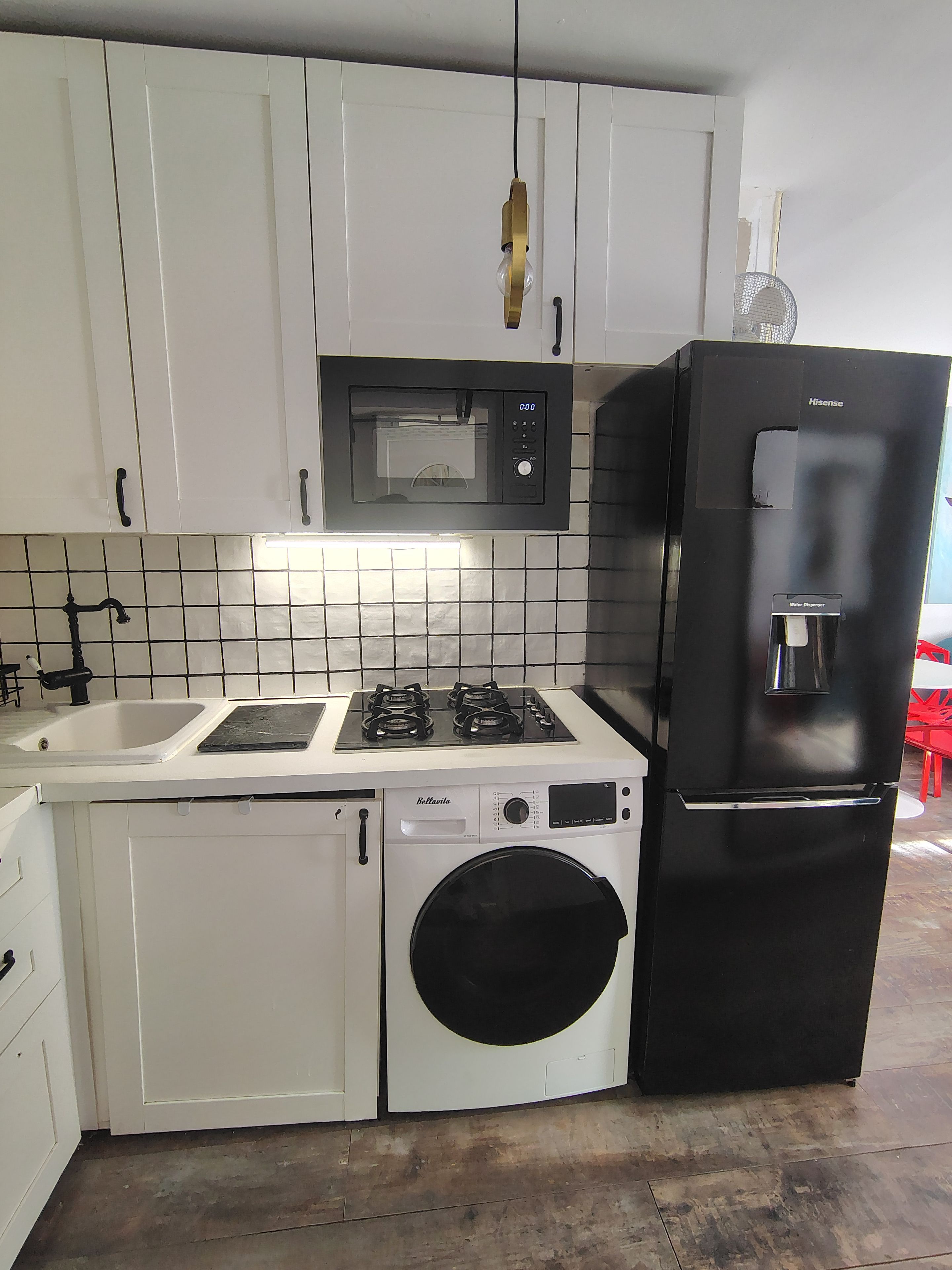 A compact kitchen with a microwave, stove, sink, and a water dispenser.