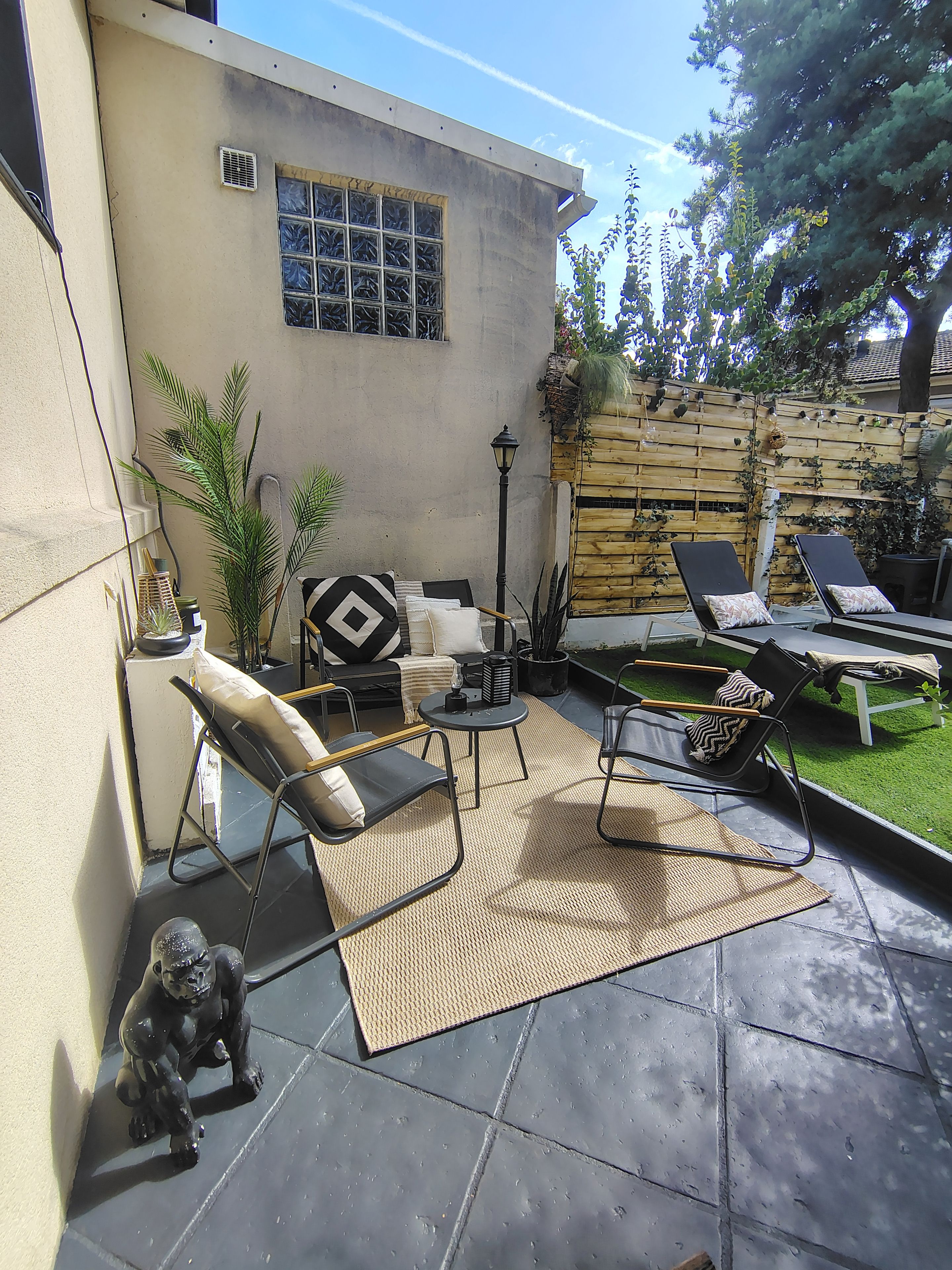 An outdoor patio area with a concrete floor, two lounge chairs, a small table, and a decorative dog statue.