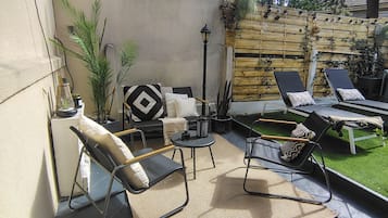 An outdoor patio area with a concrete floor, two lounge chairs, a small table, and a decorative dog statue.