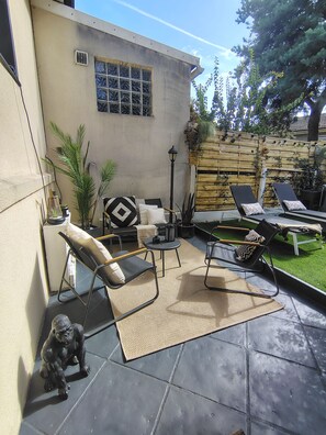 An outdoor patio area with a concrete floor, two lounge chairs, a small table, and a decorative dog statue.