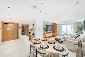 A modern living room with a dining area, a flat-screen TV mounted on the wall, and a balcony with a view. - FIRST CLASS | 2BR | High Floor | Stunning Sea View (Marina)