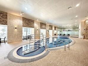 An indoor swimming pool with a glass barrier, surrounded by stone walls and a seating area with chairs. - FIRST CLASS | 2BR | High Floor | Stunning Sea View (Marina)