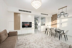 A modern living room with a flat-screen TV, a dining area with a table and chairs, and a kitchen in the background. - FIRST CLASS | Bright Luxury VILLA | Amazonia (Damac Hills)