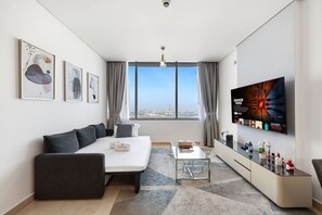 A modern living room with a sofa, a coffee table, a TV mounted on the wall, and a city view through the window. - FIRST CLASS | 1BR | Elevated Luxury | City Views (DIFC)