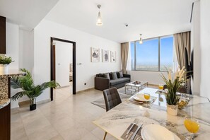 A modern living room with a sofa, dining table, and chairs, a large window with a view, and a door leading to another room. - FIRST CLASS | 1BR | Elevated Luxury | City Views (DIFC)