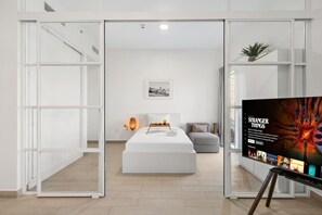 Habitació d'hotel moderna amb un llit, una taula de nit, una làmpada, un otomà gris i un cartell a la paret.