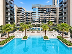 Un hotel moderno con piscina central, varios balcones y palmeras.