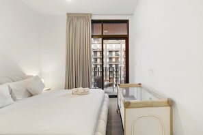 A hotel room with a bed, a window with curtains, a view of a balcony, and a small table. - FIRST CLASS | 1BR | Lavish Living | Near Downtown (Sobha Hartland)