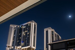 A high-rise building with illuminated signage, likely a hotel, under a night sky with a visible moon. - FIRST CLASS | 1BR | Lavish Living | Near Downtown (Sobha Hartland)