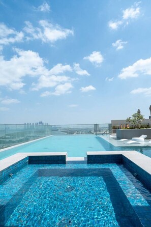 Ein Rooftop-Endlospool mit Blick auf die Stadt, umgeben von einem Glasgeländer und Liegestühlen.