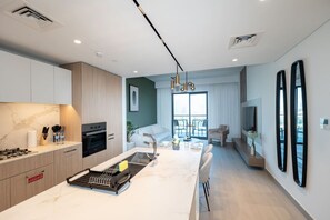 A modern kitchen with a central island, built-in oven, and a dining area with a view to the outdoors. - FIRST CLASS | 1BR| Luxe Urban Living (Sobha Hartland)