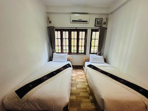 A room with two single beds, a wooden floor, an air conditioning unit, and a window with curtains. - Any Home Luxury (Luang Prabang)