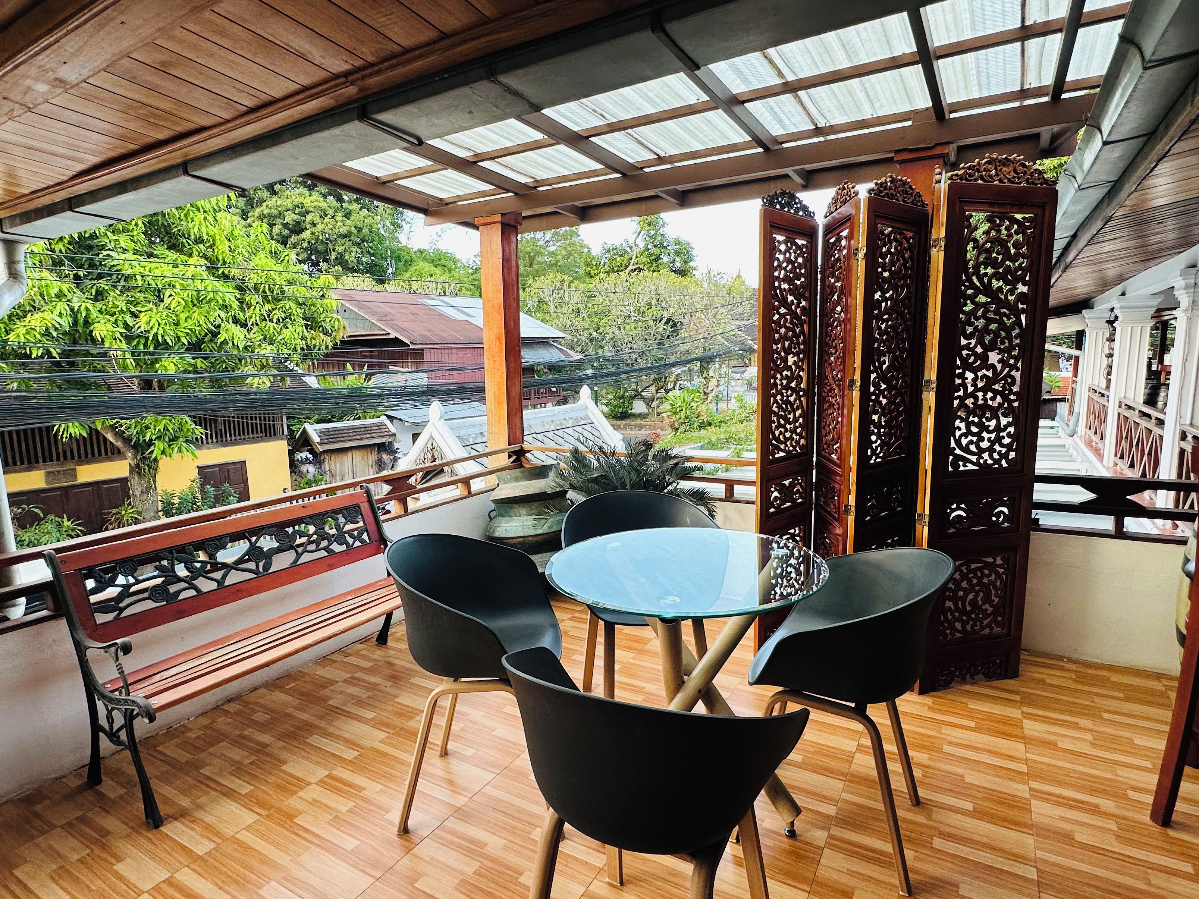 A covered outdoor seating area with a wooden floor, a round table, and black chairs.