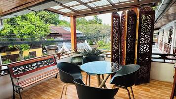 A covered outdoor seating area with a wooden floor, a round table, and black chairs.