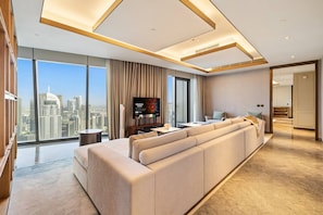 A modern living room with a large sofa, a flat-screen TV, and a city view. - FIRST CLASS | 5BR | Burj Khalifa & Fountain Views (Downtown)