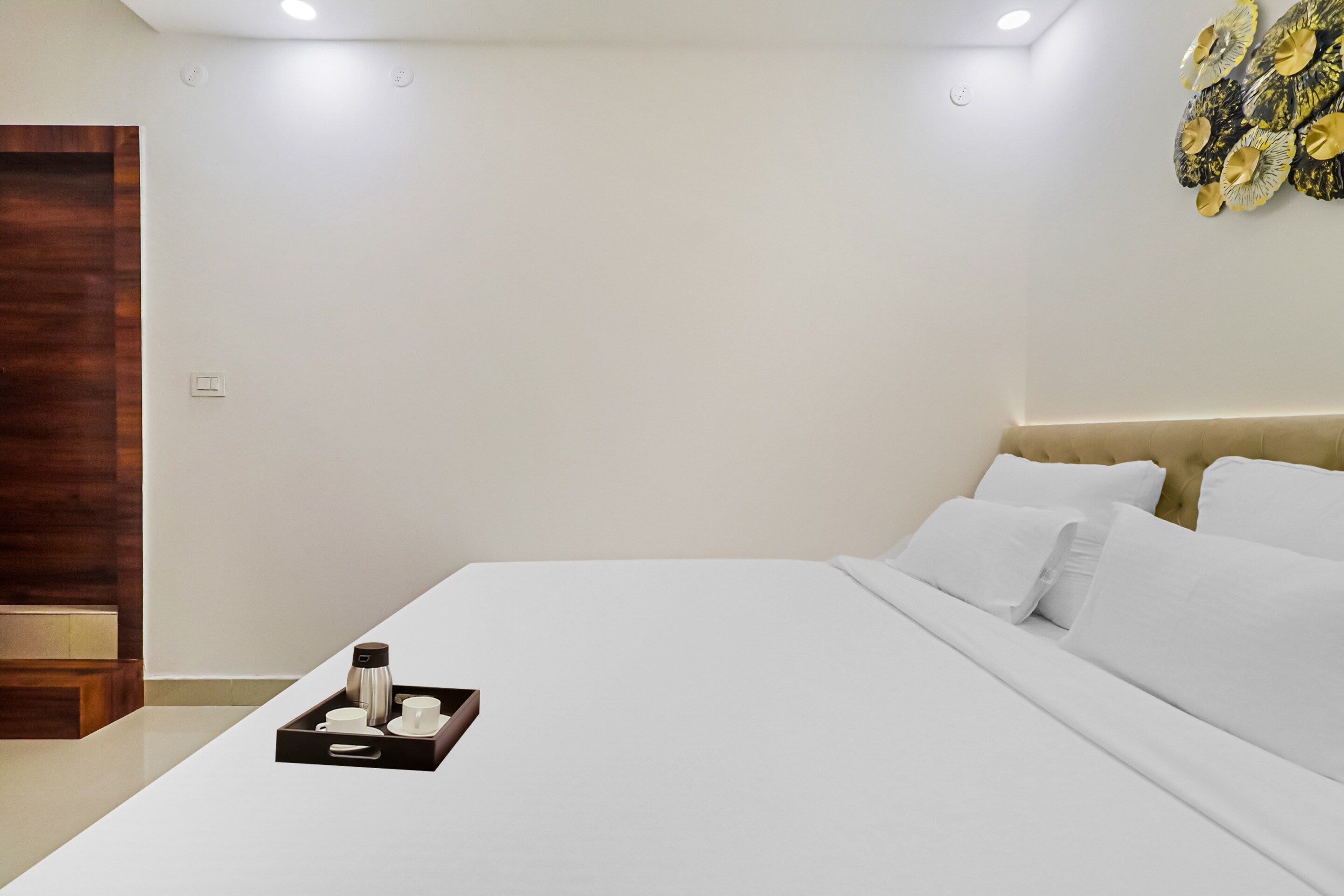 Una cama bien hecha con sábanas blancas, una bandeja con cafetera y tazas, y un cabecero de madera.