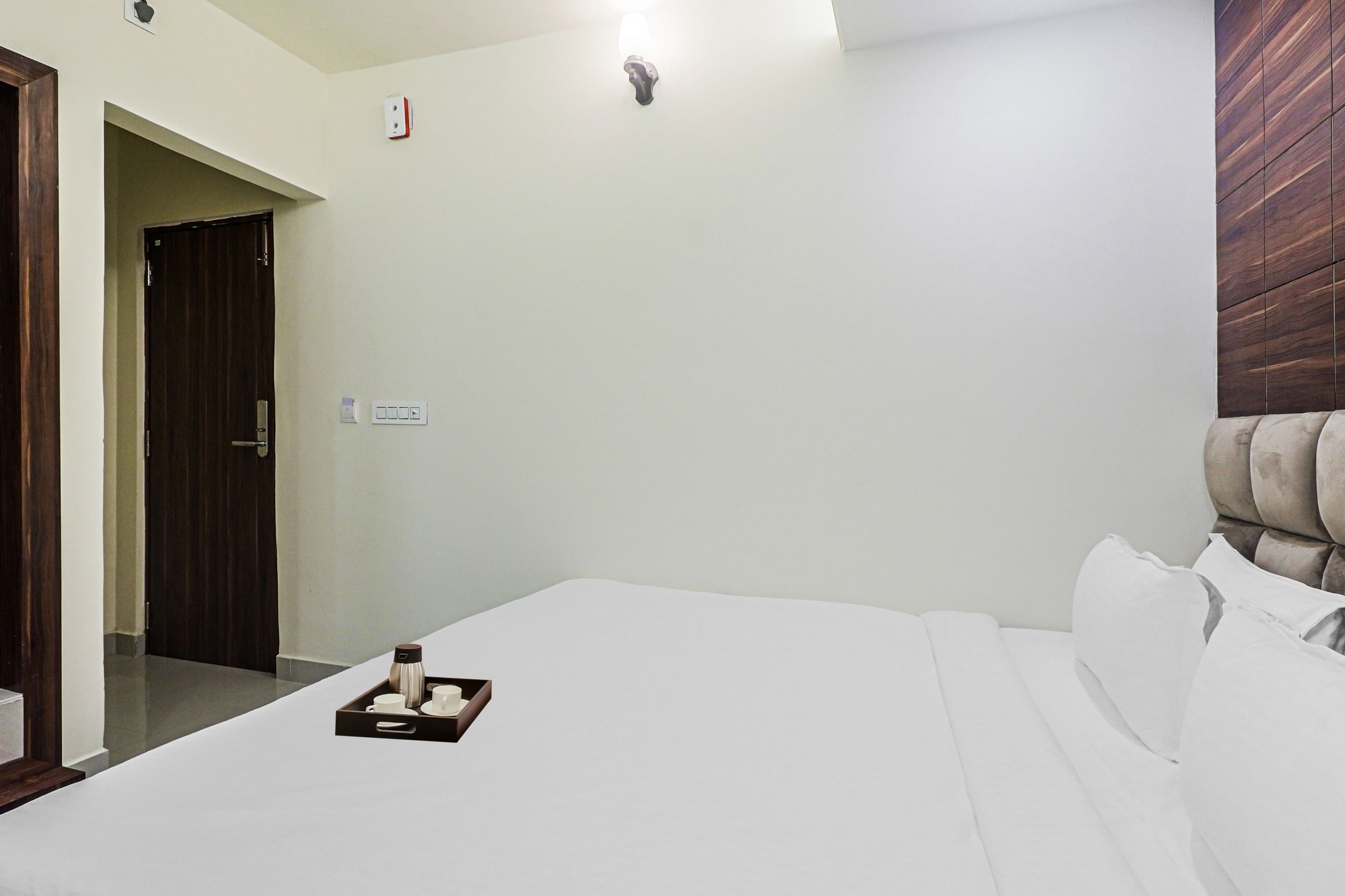 Una habitación de hotel con una cama, una mesita de noche con una bandeja de objetos, un cabecero de madera y una puerta.