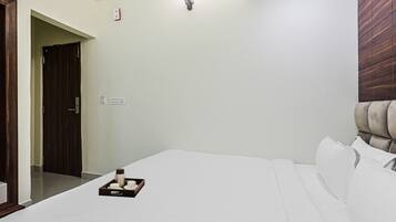 Una habitación de hotel con una cama, una mesita de noche con una bandeja de objetos, un cabecero de madera y una puerta.