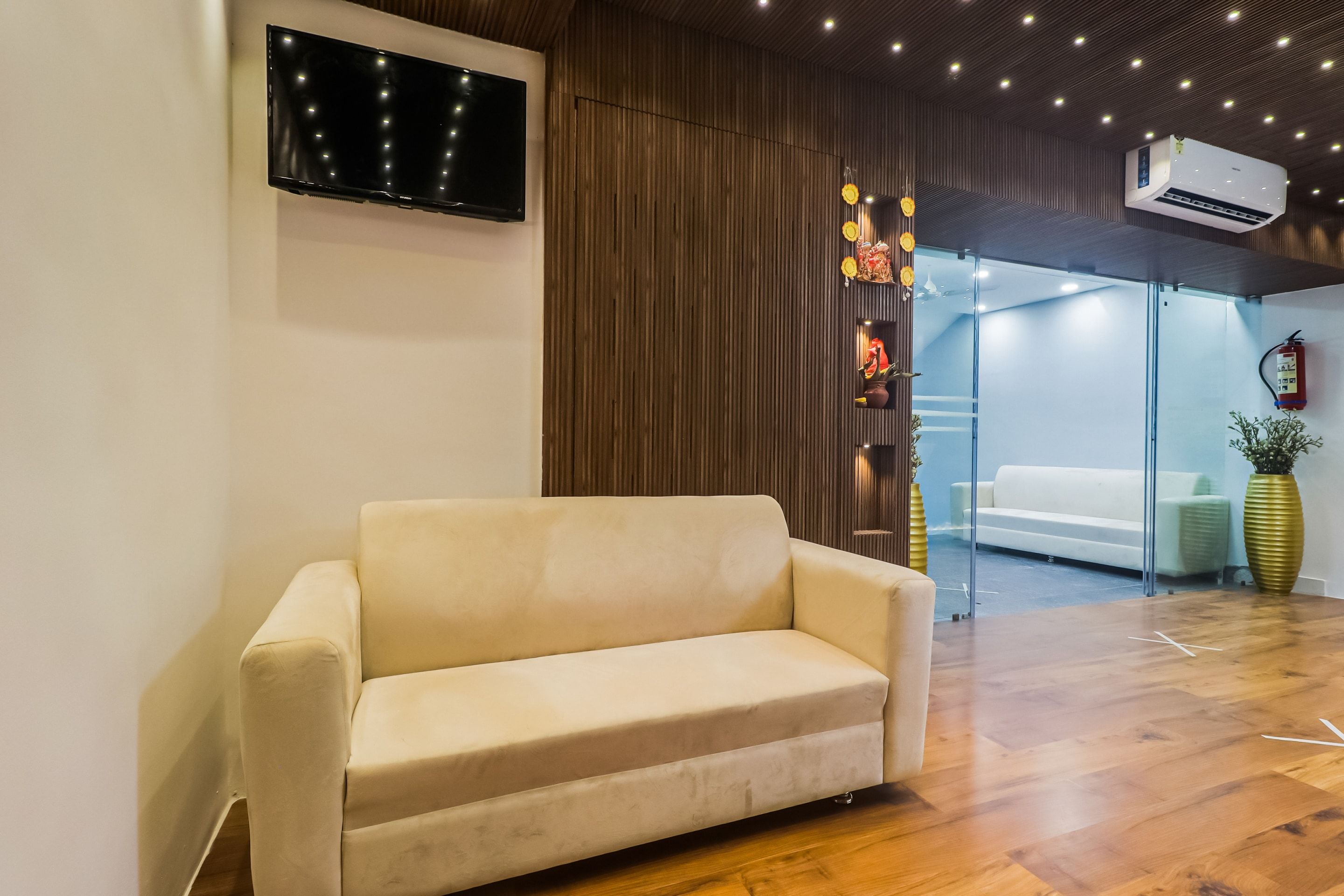 Un interior moderno con sofá, televisor de pantalla plana, paneles de madera y una división de vidrio.