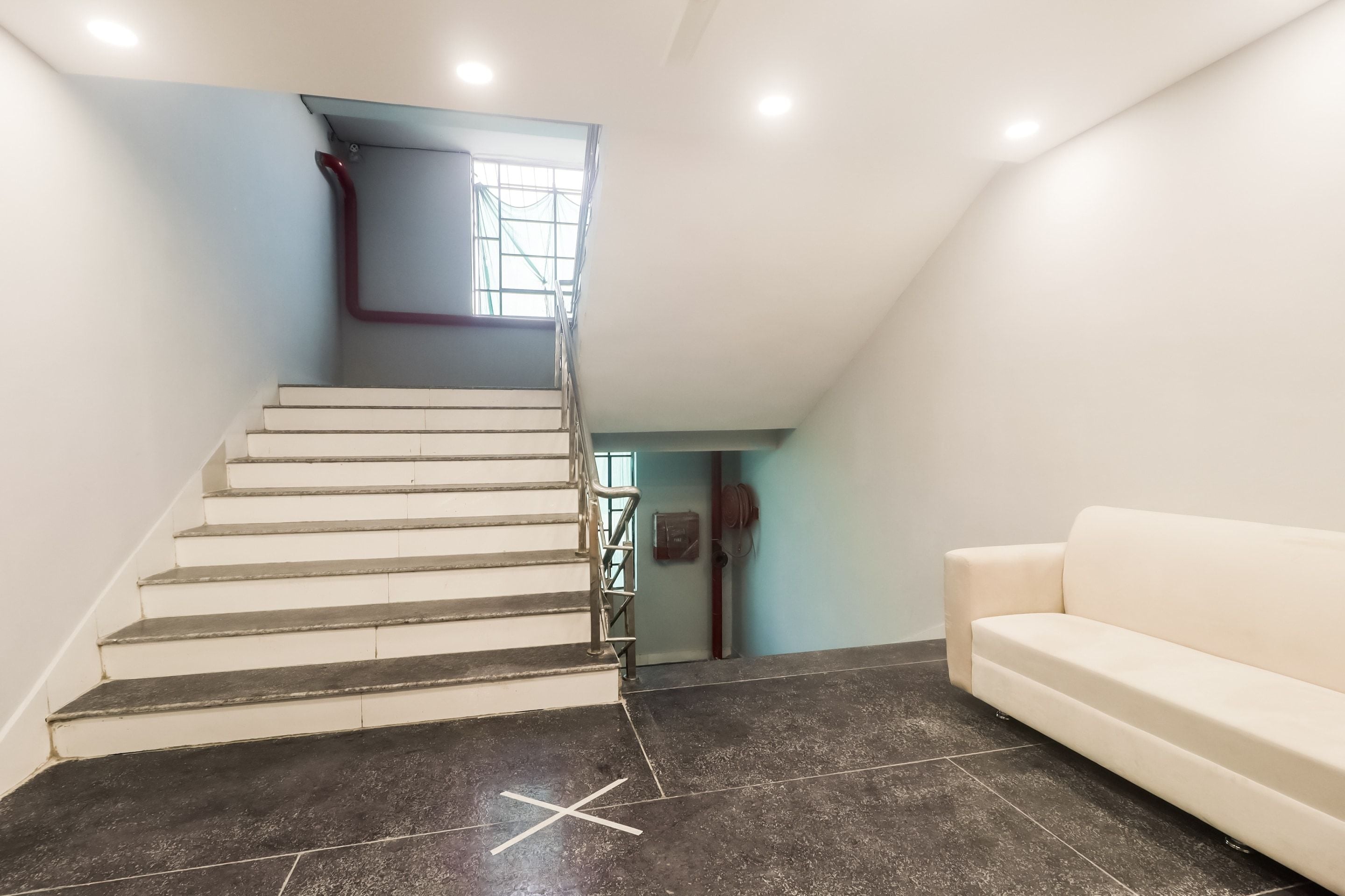 Una escalera conduce a un dormitorio en la mezanina, con un sofá blanco y una ventana.