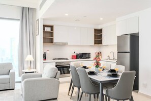 A modern kitchen with white cabinets, a black refrigerator, and a dining area with a table set for four. - FIRST CLASS | 2BR | Prime Downtown | City Views (Downtown)