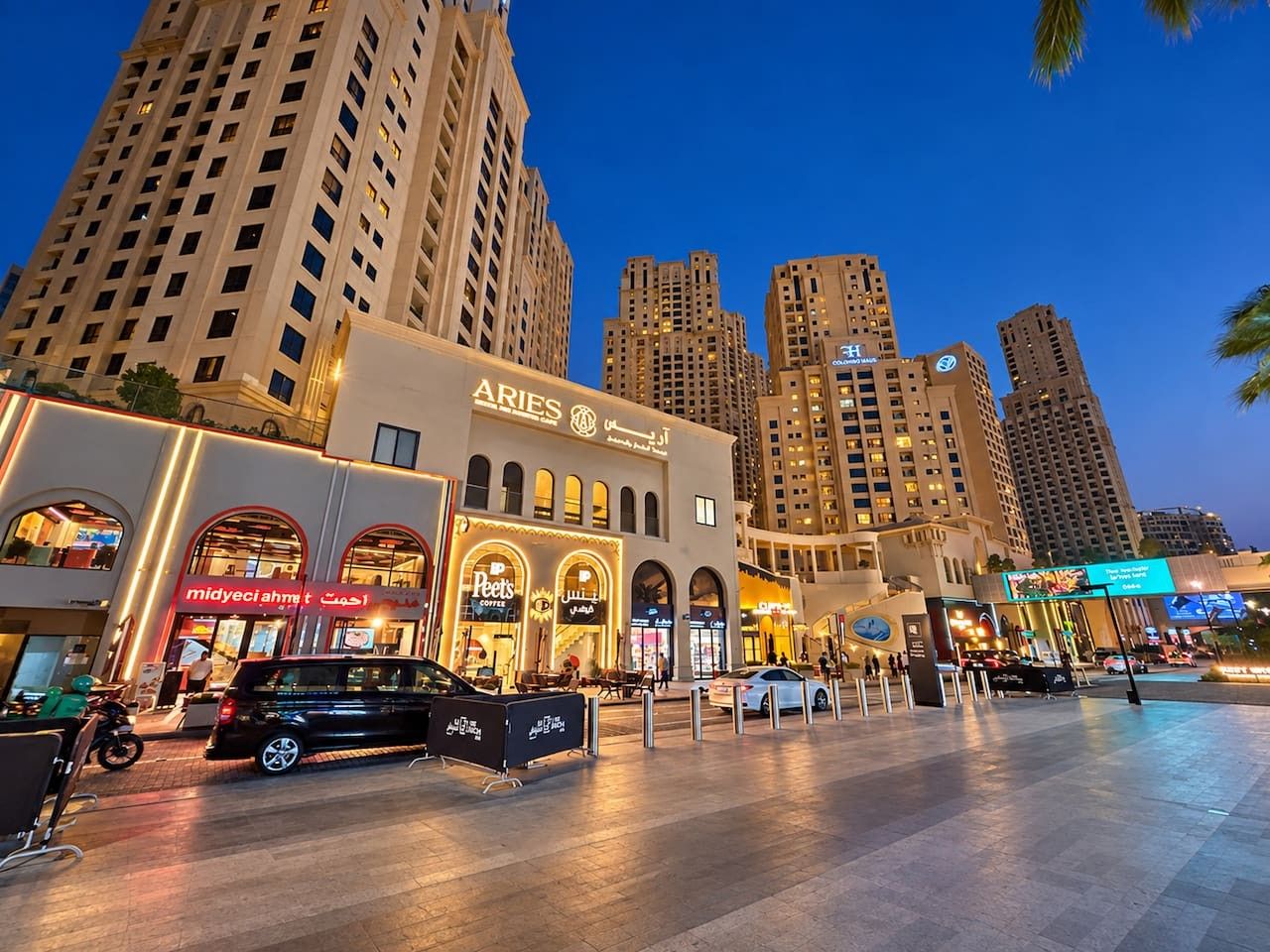 A modern hotel with a prominent sign, a spacious outdoor area, and high-rise buildings in the background.
