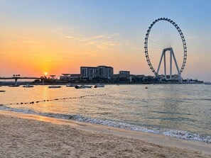Uma praia com uma grande roda-gigante e edifícios ao fundo.