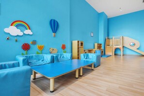 Ein Zimmer mit blauen Wänden, einer Spielecke mit Rutsche und einer Sitzecke mit blauen Möbeln.