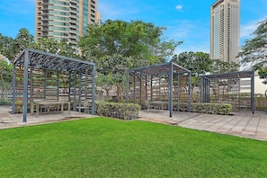 A courtyard with three pergolas, a grassy lawn, and a cityscape in the background. - FIRST CLASS | 3BR | Burj Khalifa & Fountain Views (Dubai)