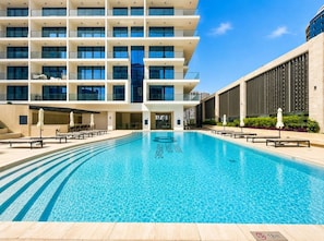 A modern hotel with a swimming pool, multiple floors, and outdoor seating areas. - FIRST CLASS | 1BR | Canal View | Near Downtown (Business Bay)