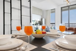 A dining area with a table set for two, a fruit bowl, and two glasses of orange juice. - FIRST CLASS | 1BR | Warm & Stylish Retreat (Dubai Production City)